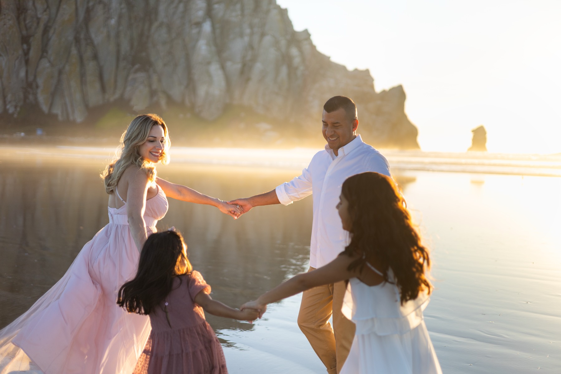 Family holding hands and dancing at golden hour in front of Morro Rock