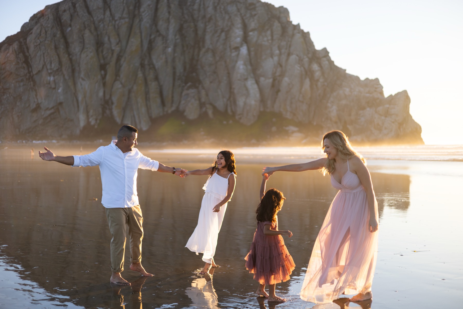 Family holding hands in a line at golden hour by Morro Rock