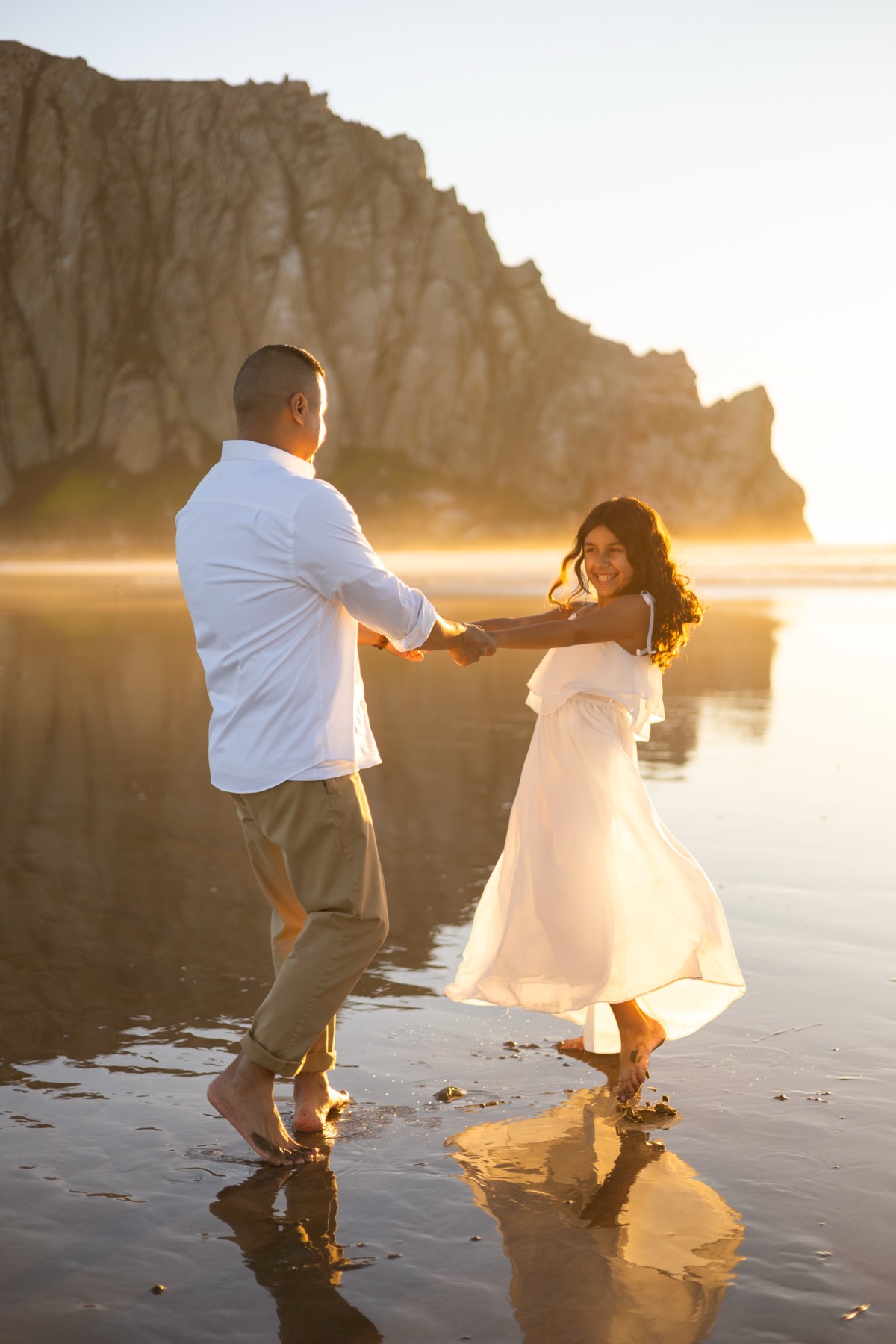 Dad twirling his daughter at sunset in front of Morro Rock