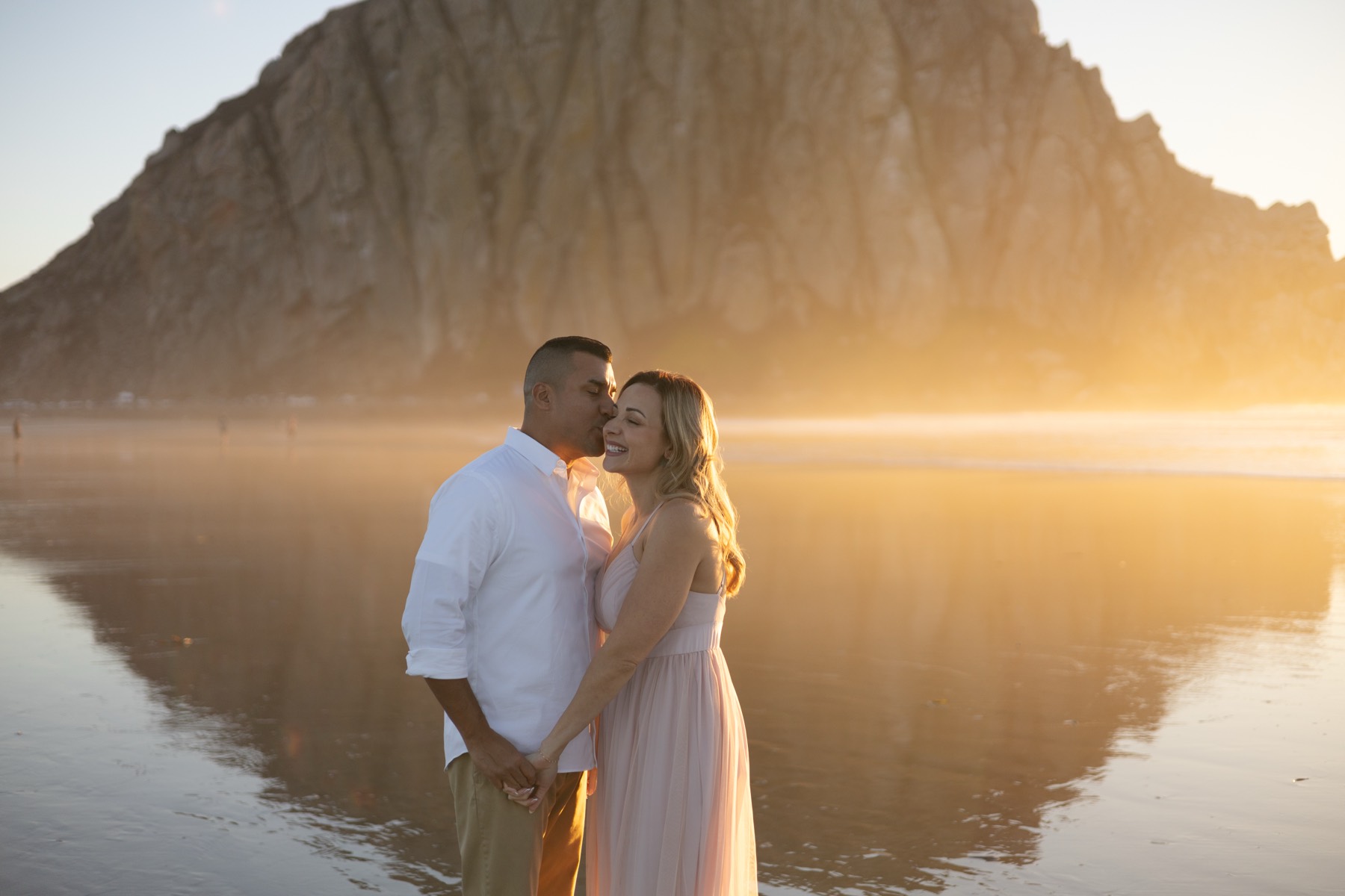 Couple sharing a kiss at golden hour in front of Morro Rock
