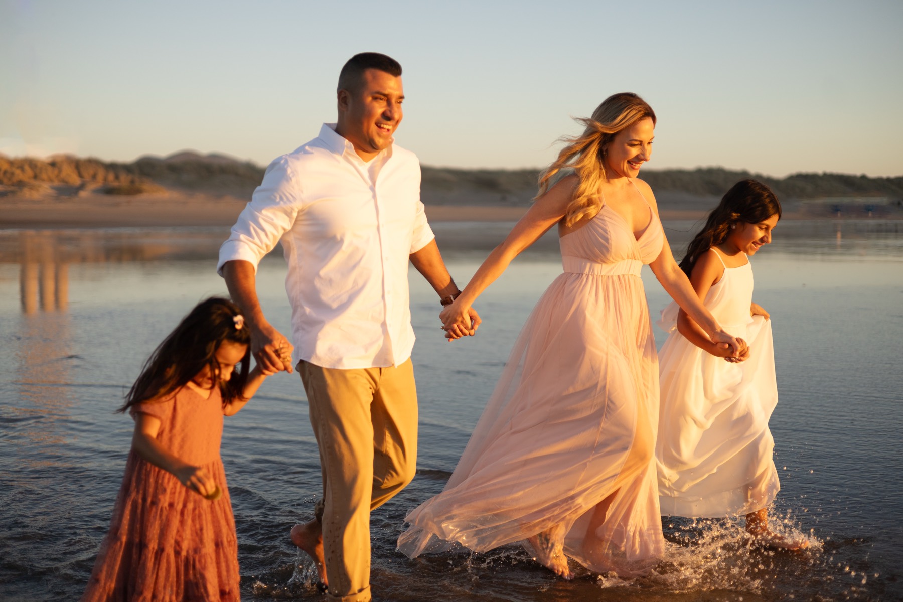 Family running through the waves at sunset