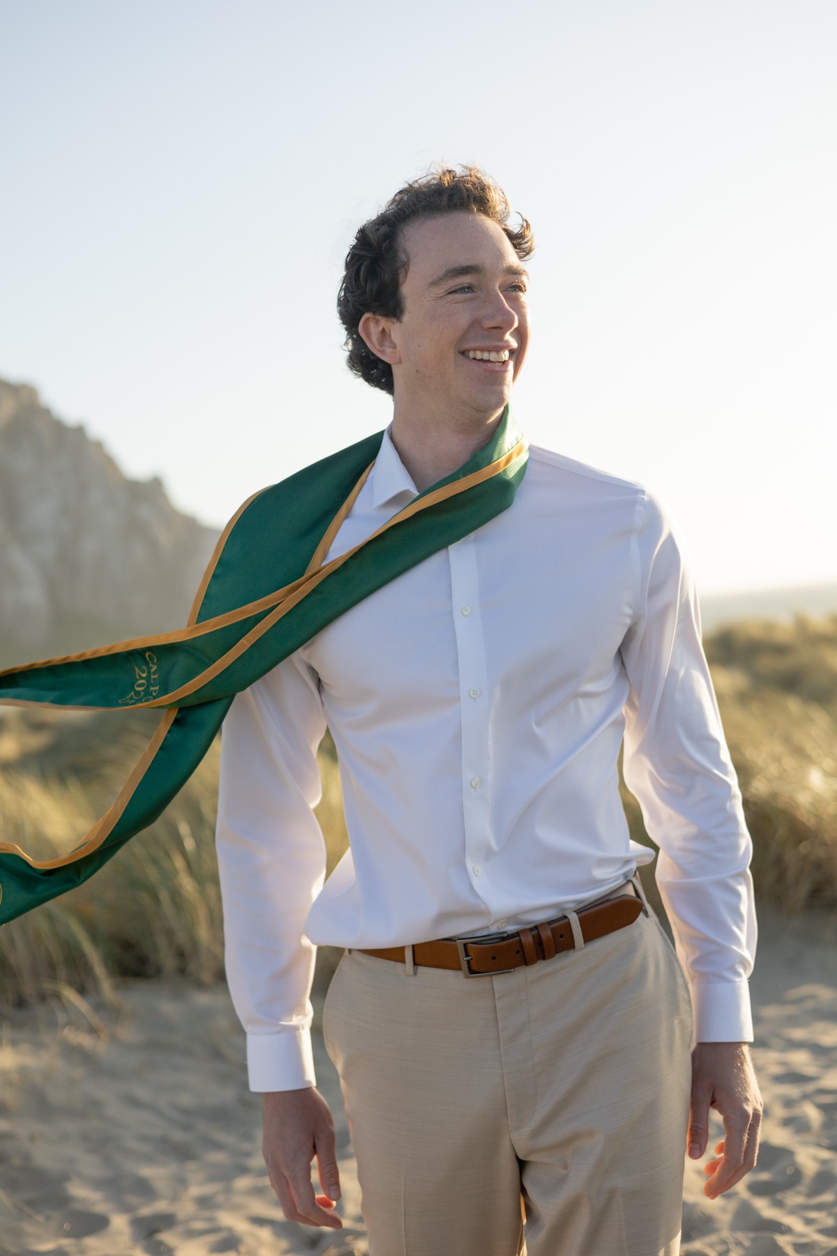 Graduate laughing on the dunes as his stole flies in the wind
