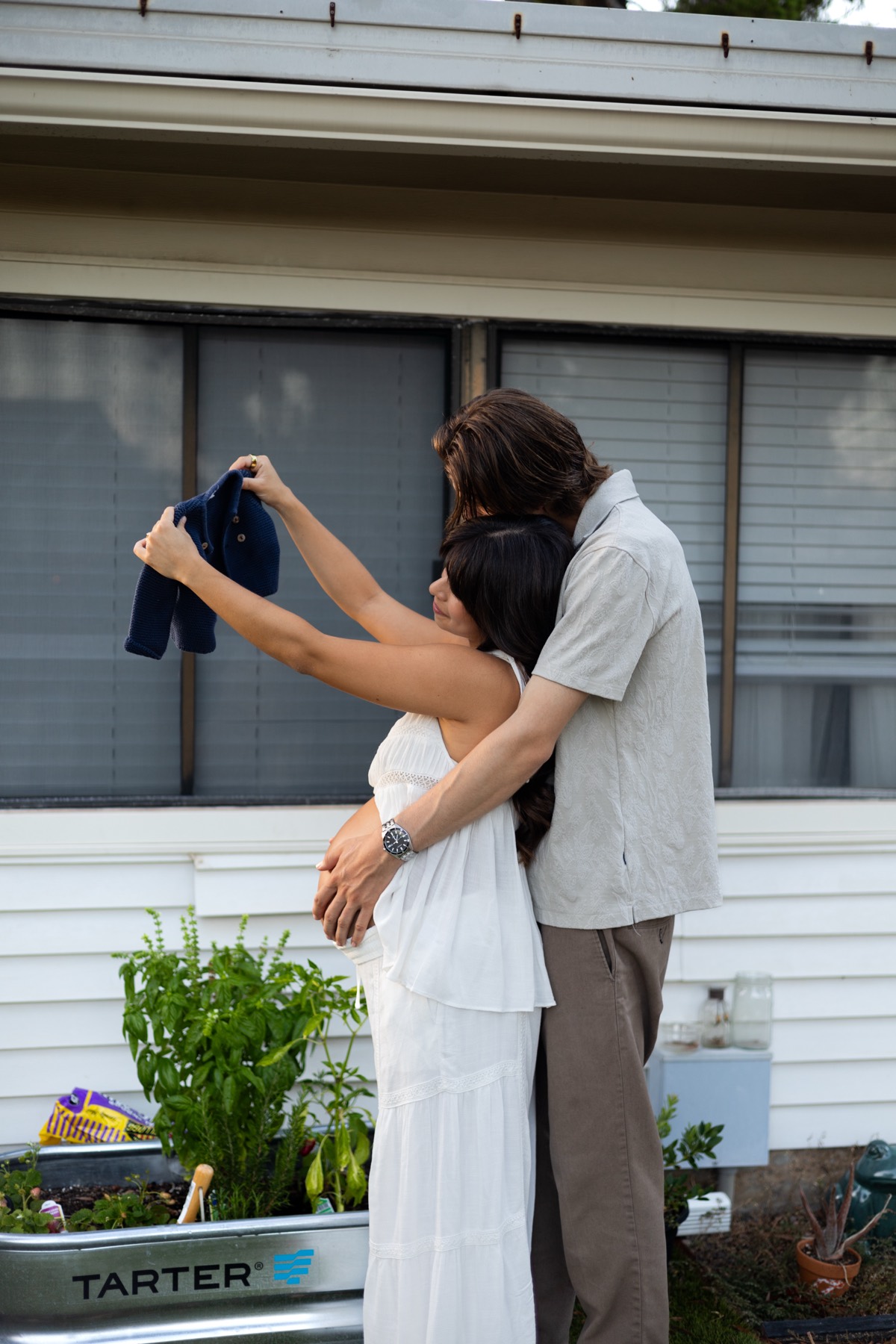 Expecting couple holding up tiny baby clothes