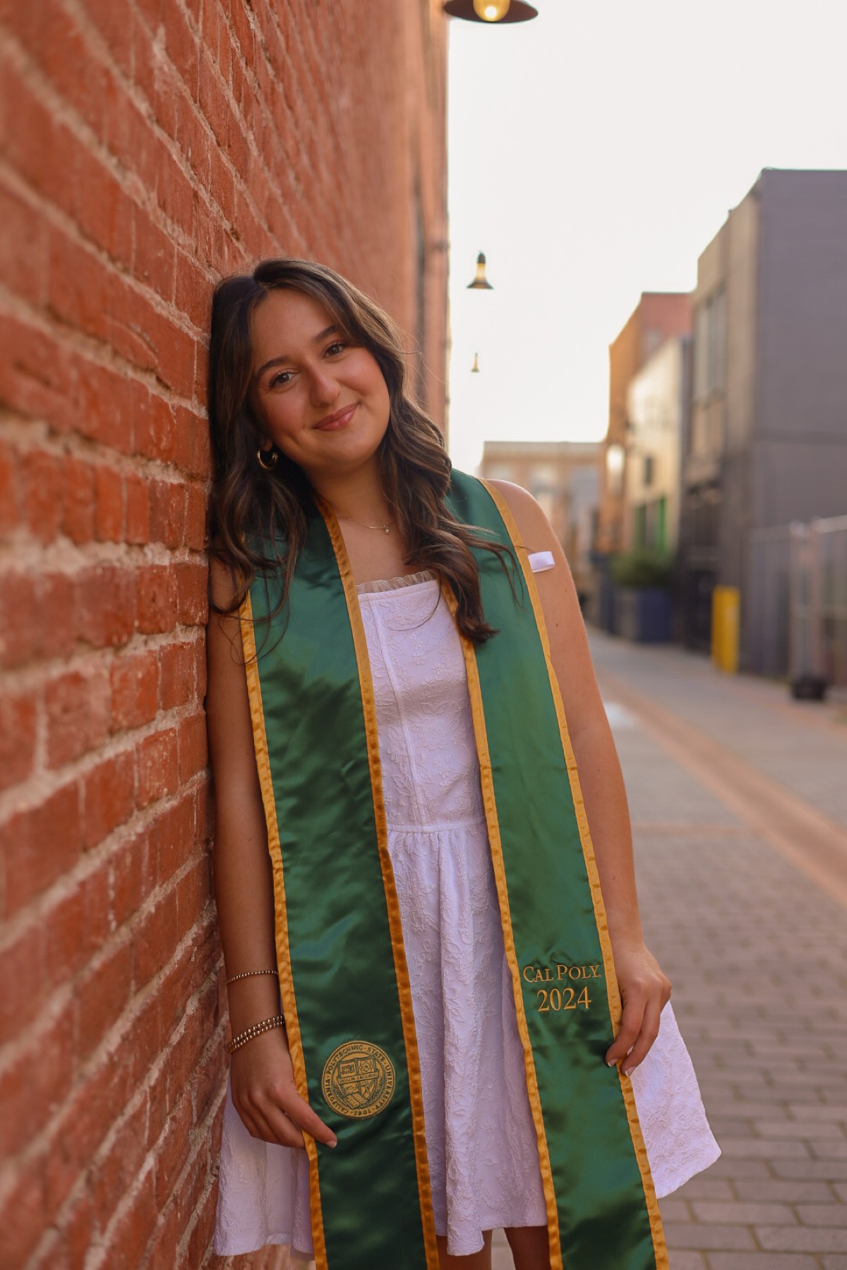 Graduate in a green stole leaning against a brick wall