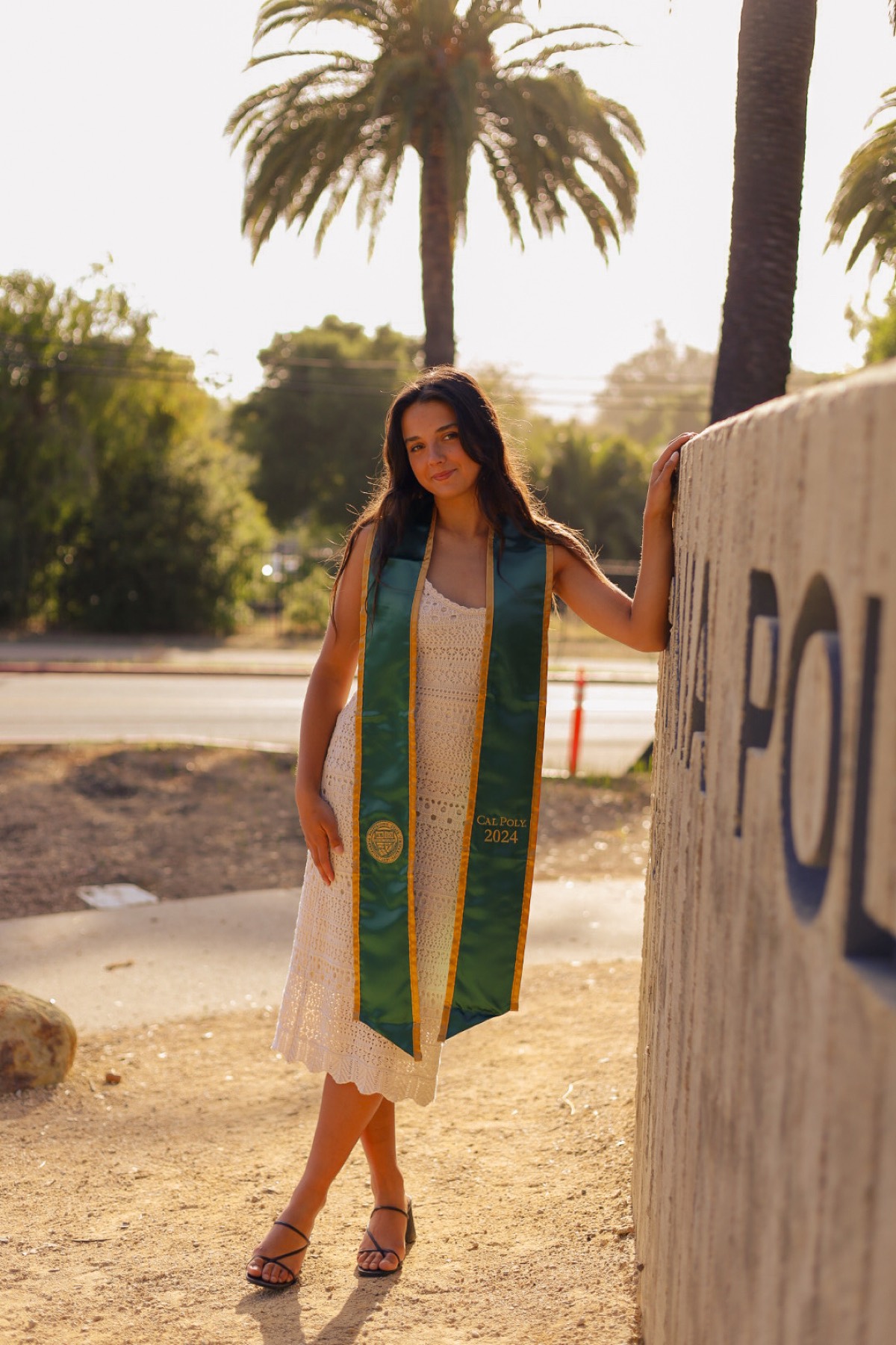 Cal Poly graduate by the Cal Poly wall at golden hour