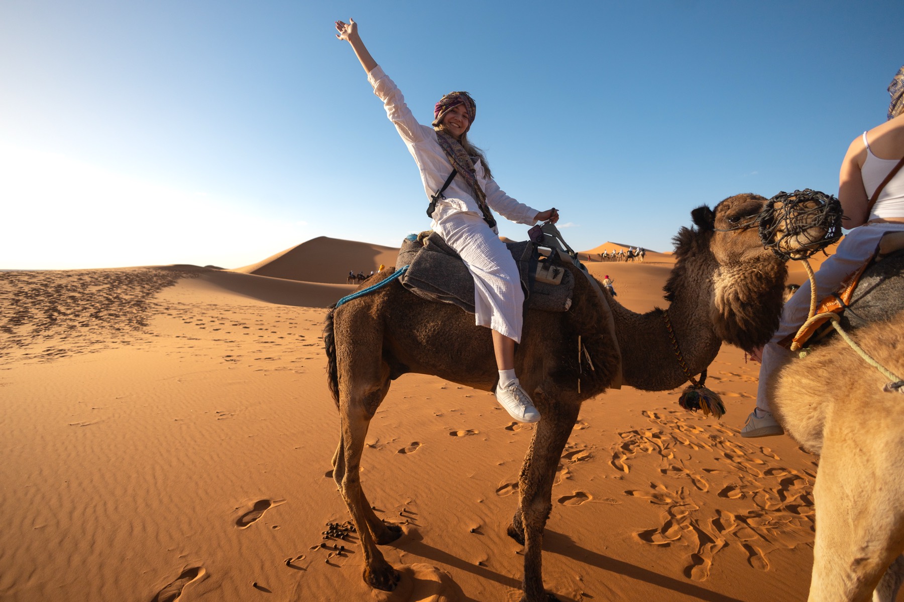 Olivia riding a camel across the desert, one arm in the air